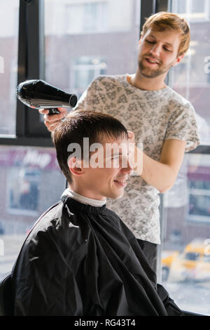 Young hipster guy in barber shop, hairdresser cutting hair with scissors, blow-drying. Concept men place