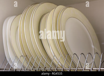 Dish drying metal rack with big nice white and light yellow clean plates on blurred background. Traditional comfortable kitchen. Stock Photo