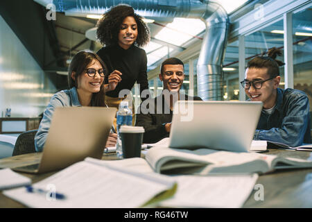 Group of young students studying together using laptop. University students smiling and using laptop in college library. Stock Photo