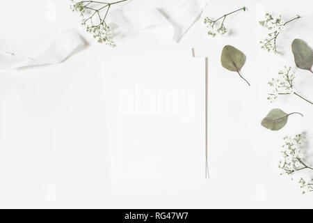 Feminine wedding styled desktop stationery mockup scene. Blank greeting card, envelope, baby's breath Gypsophila flowers, dry green eucalyptus leaves, Stock Photo