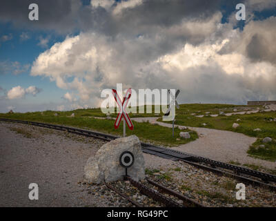 Cogwheel railway crossing with Saint Andrew's Cross near Hochschneeberg with cloudy sky in the scenic sunset, Raxalpe, Lower Austria Stock Photo