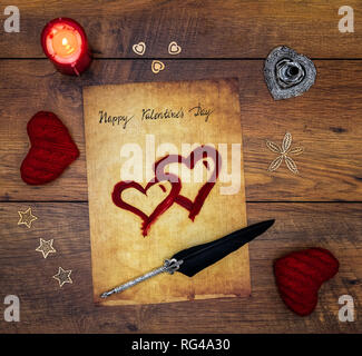 Classic Happy Valentine’s Day card hand written on parchment 2 red painted heart red candle decorations silver quill and stand on vintage oak top view Stock Photo