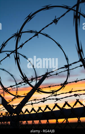Dramatic sunset with chain link fence and razor wire silhouette. Stock Photo