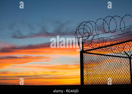 Dramatic sunset with chain link fence and razor wire silhouette. Stock Photo