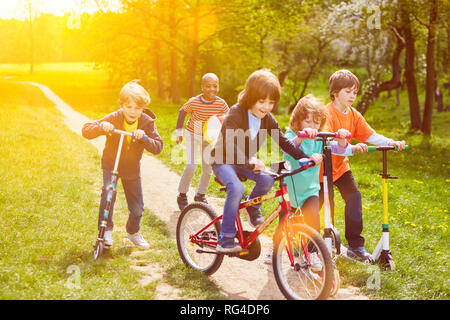 Playing children ride together with scooter and bike in the park Stock Photo