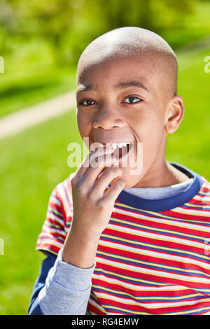 African boy mischievously smiles in the park in the summer. Vacation in the sunshine Stock Photo