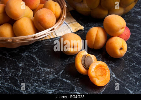 Ripe organic apricots harvested at summer time and big glass jar with canned sweet apricot compote on dark marble. Composition in rustic style - organ Stock Photo