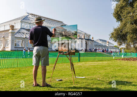 An artist paints on an easel the newly renovated Temperate House in Kew Gardens, Richmond upon Thames, London, England, UK. Stock Photo