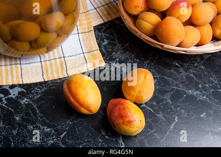 Ripe organic apricots harvested at summer time and big glass jar with canned sweet apricot compote on dark marble. Composition in rustic style - organ Stock Photo
