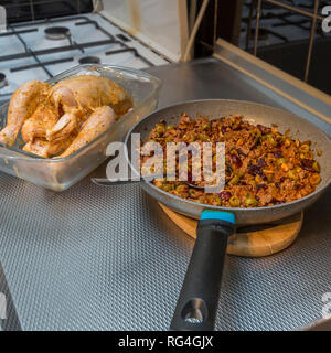 image of a fresh and raw whole chicken spread with butter and next to a pan with ground beef prepared with olives, raisins, walnuts Stock Photo
