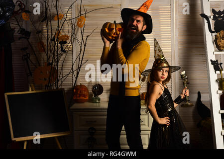 Little girl in wizard hat and man with halloween pumpkin. Little girl witch and wizard man celebrate halloween. We love the spirit of Halloween and Stock Photo