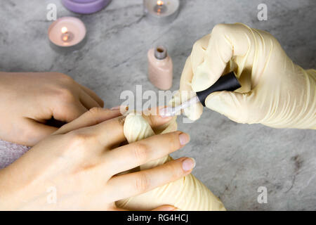 close up hands of manicurist in gloves  holding hands of client, to  apply transparent nail polish on healthy natural woman's nails,  process of manic Stock Photo