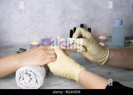 close up hands of manicurist in gloves  holding hands of client, to  apply red nail polish on healthy natural woman's nails,  process of manicure and  Stock Photo