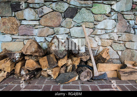 Firewood stocked next to Ax in front of Stone Wall Stock Photo