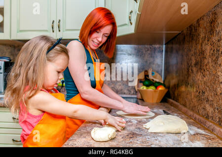 Mom and little cute girl in orange aprons, smiling and making homemade pizza, roll out the dough at home in kitchen. Concept happy family holiday, Ita