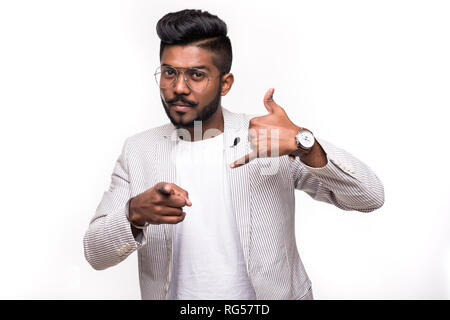 Call me back please. Young attractive hipster indian man, makes phone sign, indicates with index finger directly at camera, wants to speak with someon Stock Photo