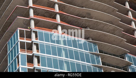 Construction of a new high rise building with a construction crew member working on the edge of the building.  Bright blue sky. Stock Photo