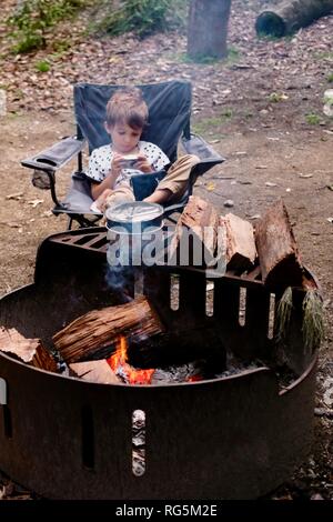 A young girl sits near a campfire, Fern flat campsite area, Eungella National Park, Queensland, Australia Stock Photo