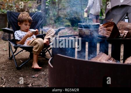 A young girl sits near a campfire, Fern flat campsite area, Eungella National Park, Queensland, Australia Stock Photo