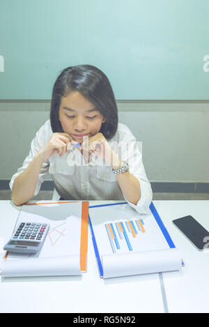 Young Asian office employee checking sales reports at workplace Stock Photo