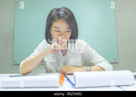 Young Asian office lady checking information on sales reports Stock Photo