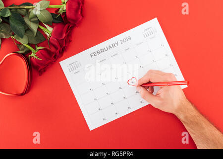 cropped view of man marking with heart 14th february date on calendar isolated on red, st valentines day concept Stock Photo