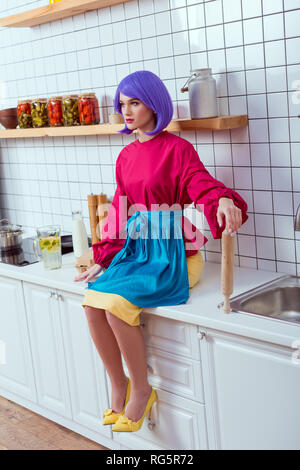 selective focus of housewife with purple hair sitting on kitchen counter with rolling pin Stock Photo