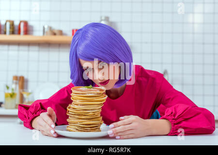 beautiful housewife with purple hair looking at plate with pancakes in kitchen Stock Photo