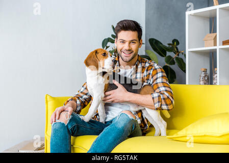 handsome smiling man sitting on sofa with beagle dog Stock Photo
