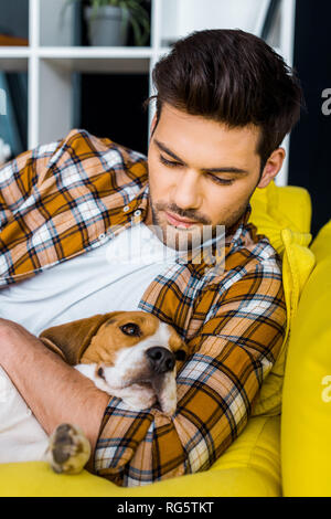 handsome man in checkered shirt resting on sofa with dog Stock Photo