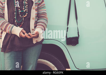 no recognizable face woman using phone technology messaging with blue vintage van in the background and retro camera on the side - travel and hippy co Stock Photo