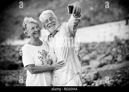 Black and white image retro concept filter - couple of happy smiling cheerful aged elderly people taking selfie picture with modern smart phone to sha Stock Photo