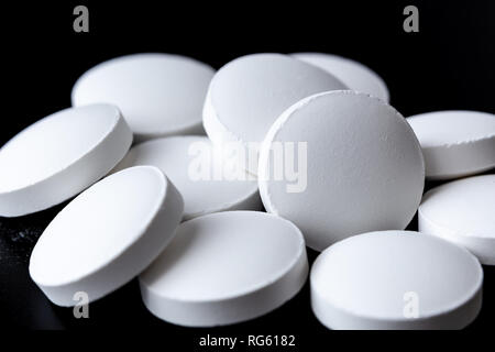Heap of white pills on black background close up