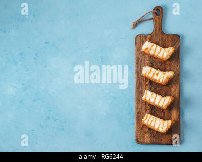 caramelized cheesecake slices on wooden cuttingboard. Cheesecake on blue background with copy space for text. Top view or flat lay.