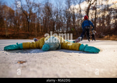 Girl lying on a frozen pond with her arms outstretched and two people, ice-skating in the background, United States Stock Photo