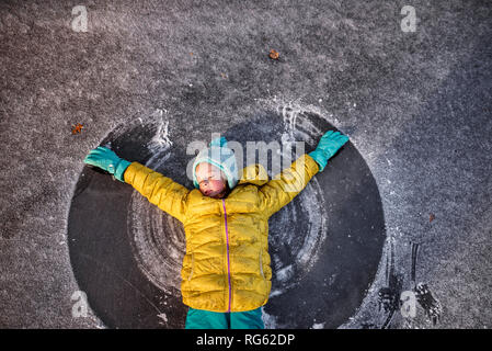 Girl lying on a frozen pond making a snow angel with her arms, United States Stock Photo