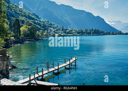 Woman is posing at the dock on Lake Geneva, near Chateau de Chillon Castle near Montreux, Switzerland Stock Photo