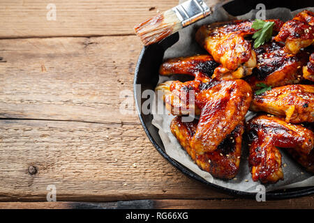 Baked chicken wings in barbecue sauce in a cast iron pan on an old wooden rustic table. Stock Photo