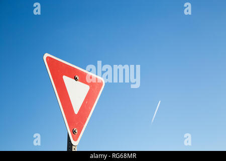 Yield sign against a blue sky with a contrail. Stock Photo