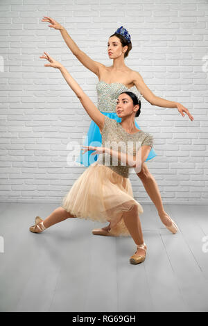 Front view of slim professional ballet dancers performing in studio. Young ballerinas in beige and blue dresses keeping hands up and looking above. Concept of ballet dance and elegance.