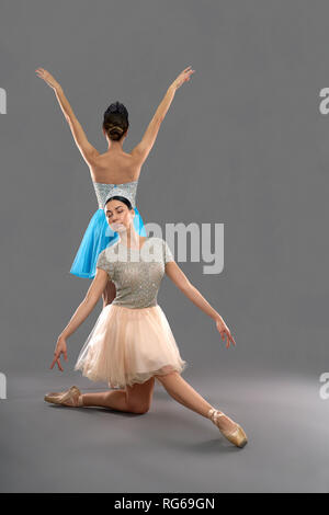 Front view of professional ballerina in beige dress sitting on knee and pointing toes while female partner in blue dress standing with back to camera and raising hands up. Concept of ballet.