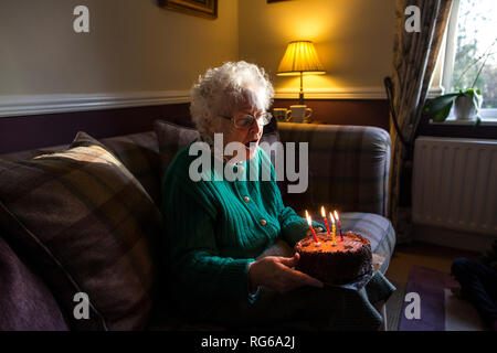 Elderly woman celebrating her birthday with a cake whilst blowing out the candles, England, United Kingdom Stock Photo