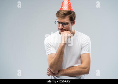 Picture of unhappy stressed young man having unhappy look, feeling tired and worn out with birthday party preparations, standing in studio. Stock Photo