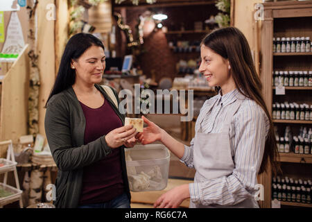Zero waste shopping - woman buying natural homemade soap at package free store. Cheerful shopkeeper helping customer in packaging free shop. Stock Photo