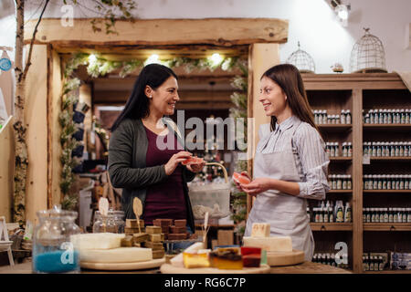 Cheerful shopkeeper helping customer in packaging free shop. Zero waste shopping - woman buying natural homemade soap at package free store. Stock Photo