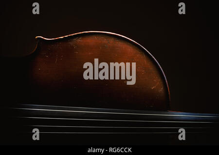 Part of an old dusty cello, details of old wood and strings, accentuated shapes in dark. Stock Photo