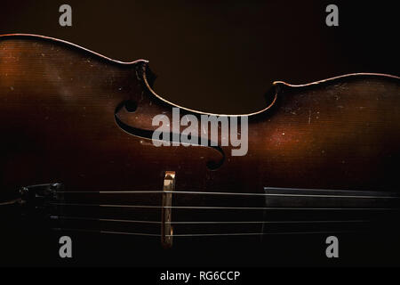 Part of an old dusty cello, details of old wood and strings, accentuated shapes in dark. Stock Photo