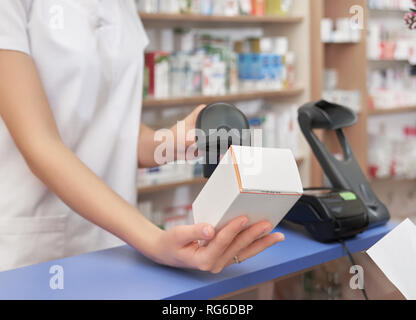 Cropped close up of pharmacist holding white medical box with medicines. Professional specialist scanning price using barcode scanner. Chemist working in drugstore. Stock Photo