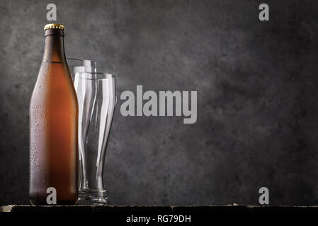 Bottle of light beer and two empty glasses on a wooden table as a human need. Food background Stock Photo