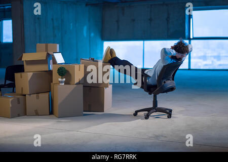 young businessman on construction site taking a break while checking documents and business workflow with cardboard boxes around him in new startup of Stock Photo
